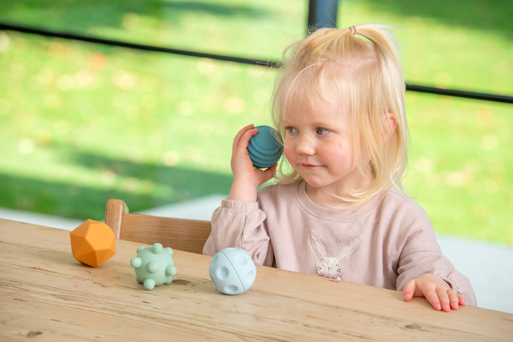 Child holding blue ribbed ball beside mint creature and orange faceted piece