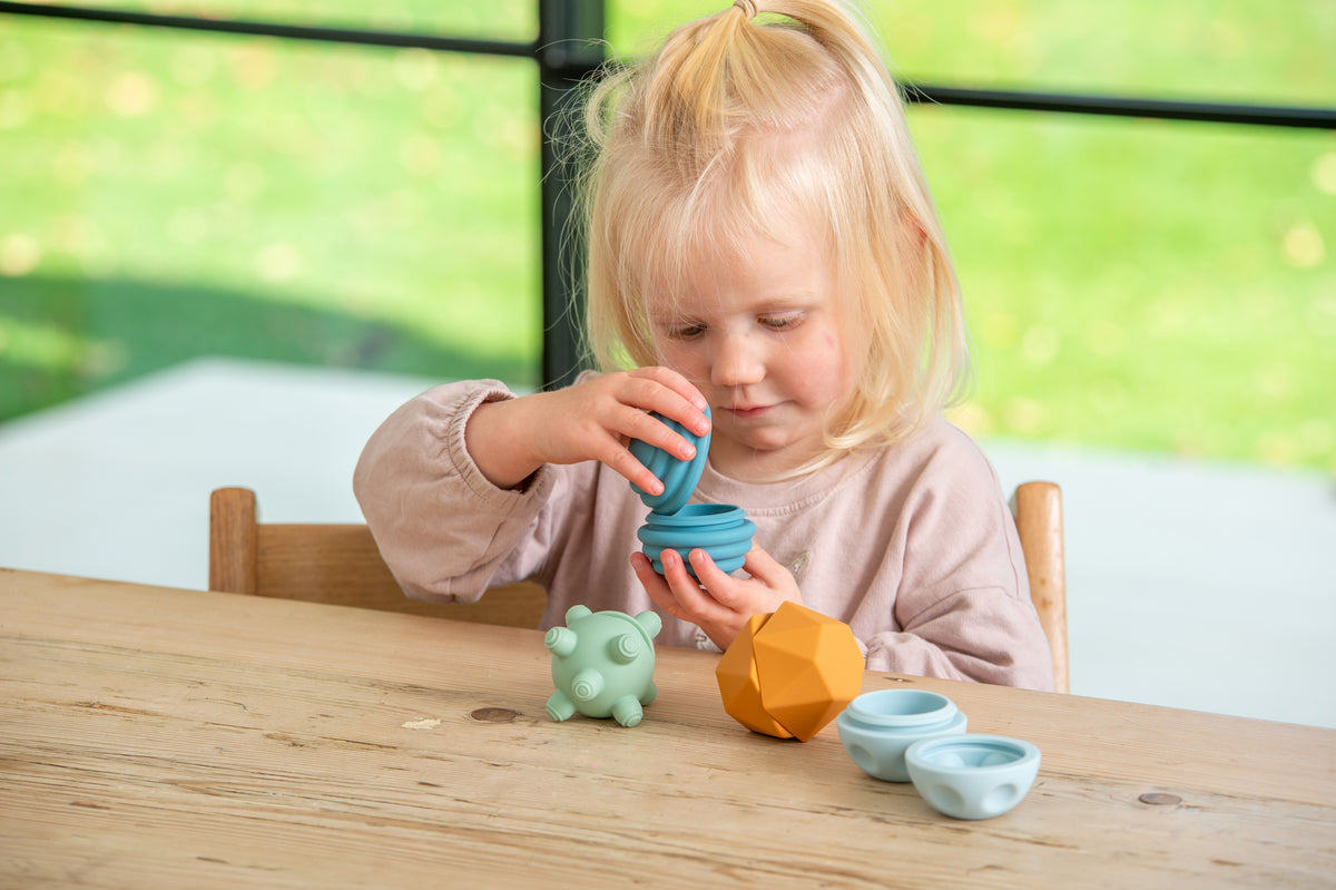 Child stacking blue ribbed balls with mint creature and orange faceted piece