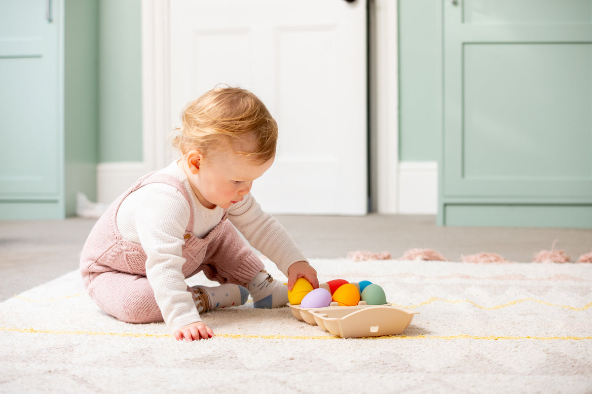 Child using beige tray to play with colorful sensory eggs on a light rug