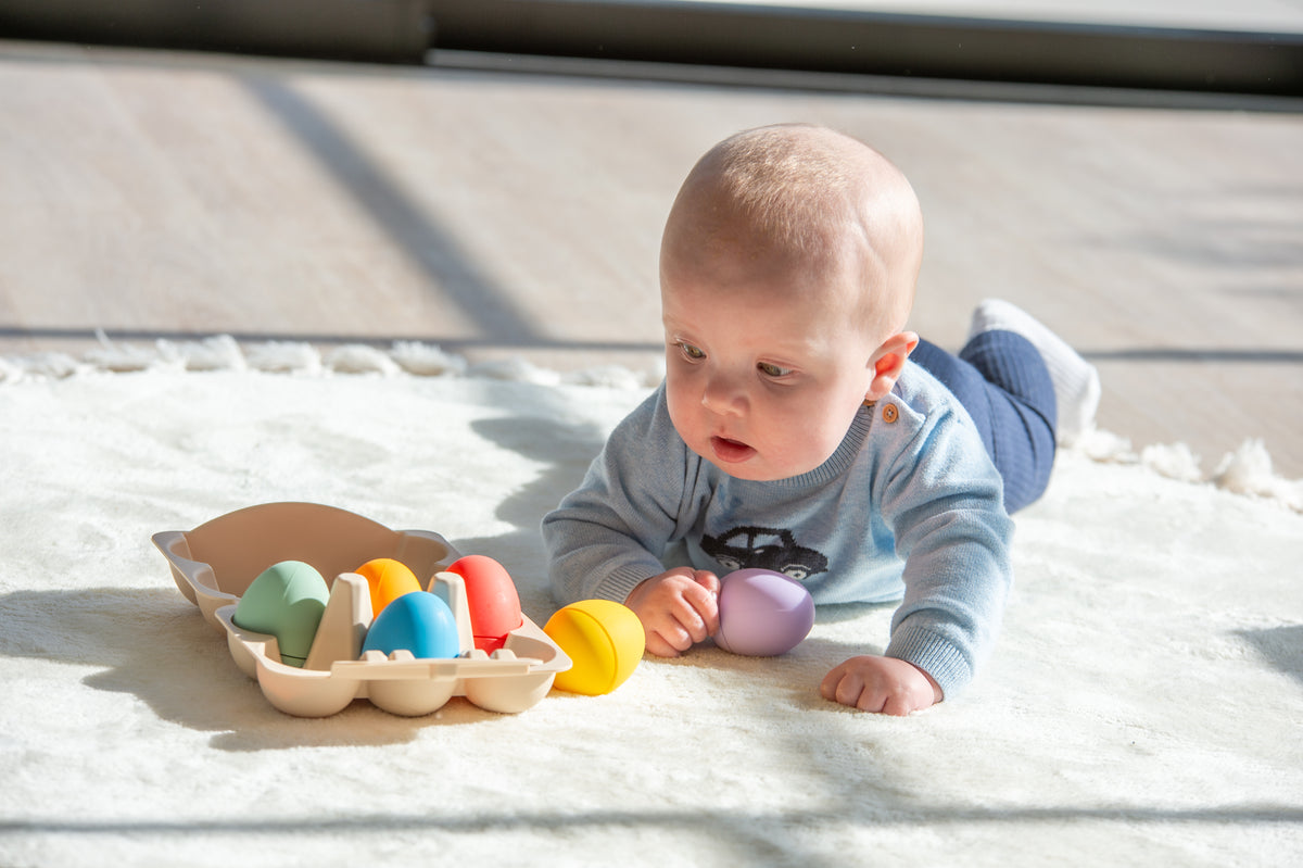 Baby playing with rainbow sensory eggs in beige tray on a soft play surface
