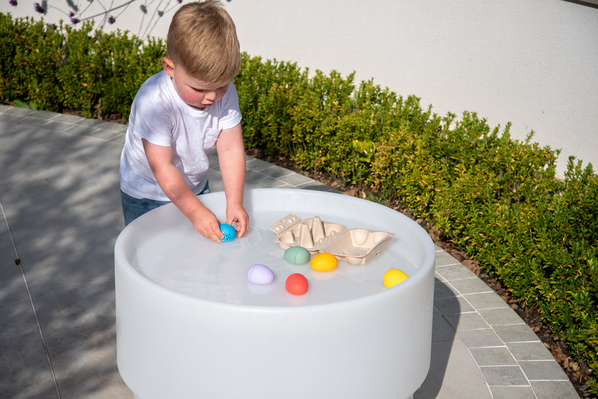 Child reaching into sensory eggs tray at a white sensory play table