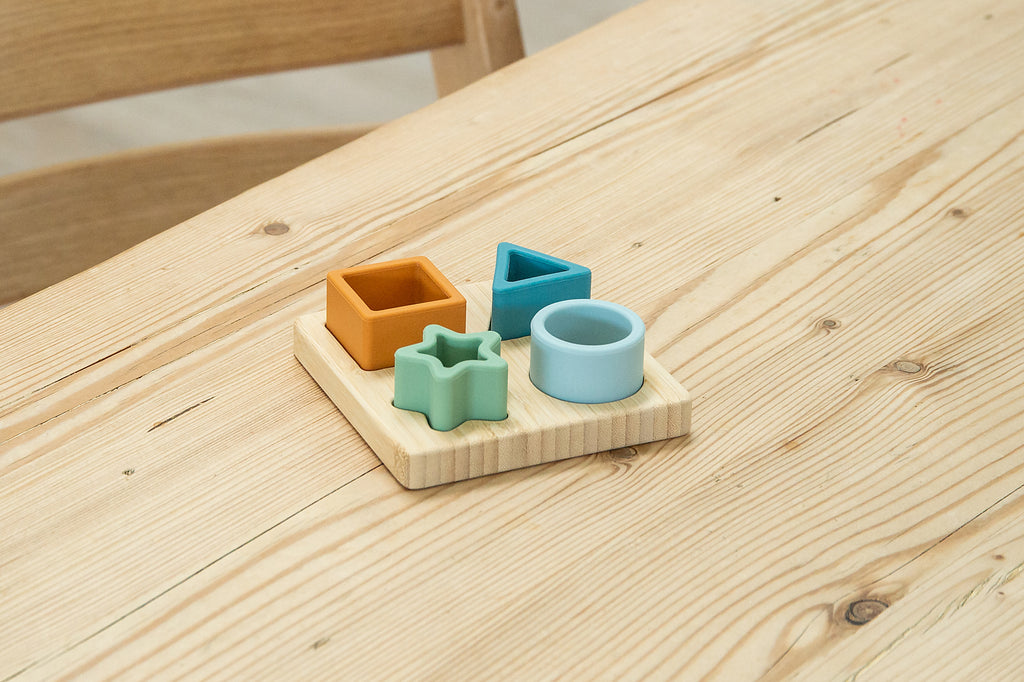 Close-up of wooden shape sorter board with orange cube, blue square, mint star, and ring
