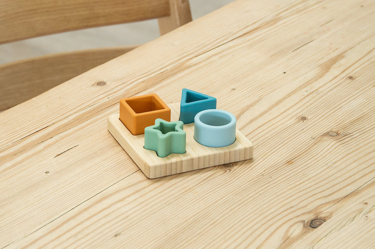Close-up of wooden shape sorter board with orange cube, blue square, mint star, and ring