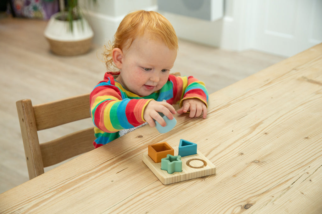 Baby using a wooden shape sorter puzzle board with pastel cube, star, and ring