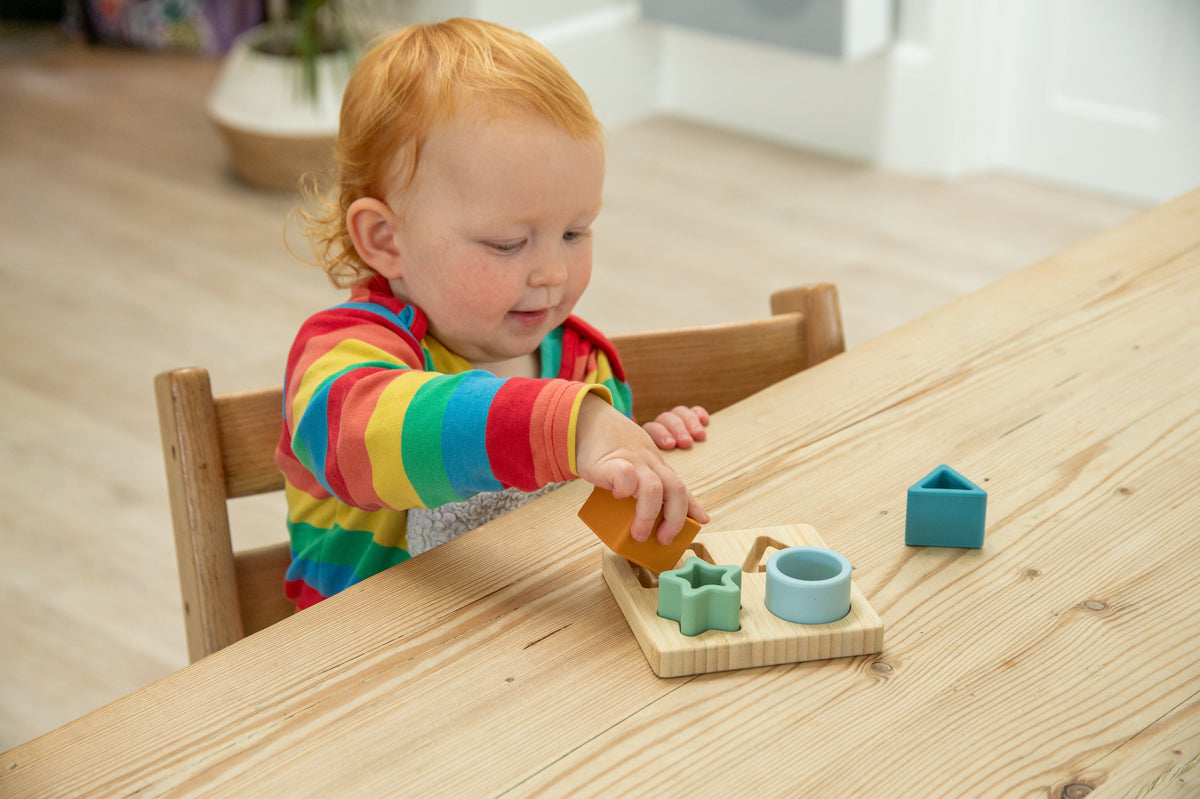 Toddler playing with a wooden shape sorter puzzle board with pastel pieces