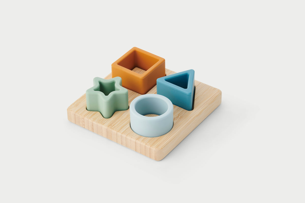 Wooden shape sorter puzzle board with star, cube, and ring pieces in pastel colors