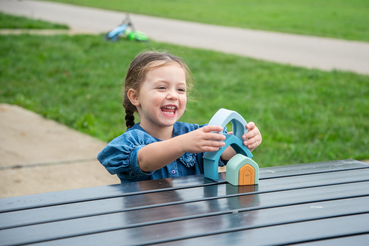 Child smiling while holding teal stacking house toy with orange door