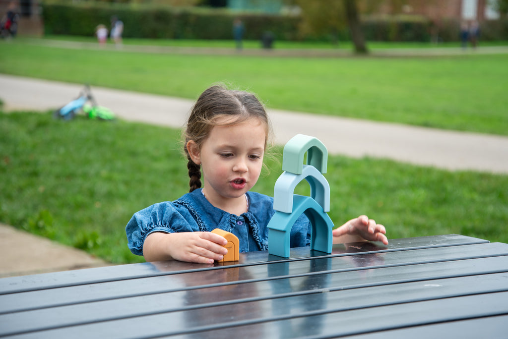 Child playing with teal stacking house toy featuring orange door and mint arches