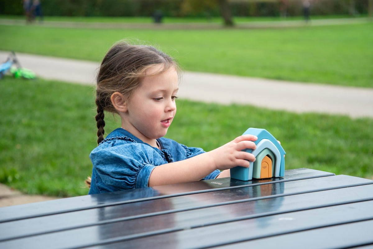 Child holding teal stacking house toy with orange door, viewed from side