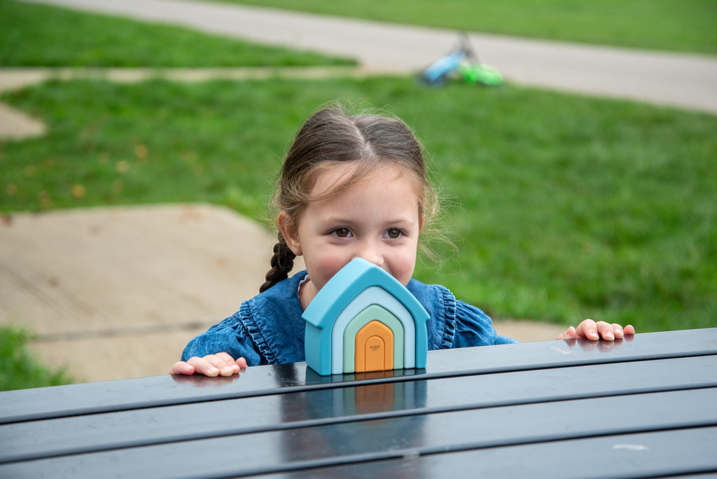 Child holding teal arch-top stacking house toy with orange door