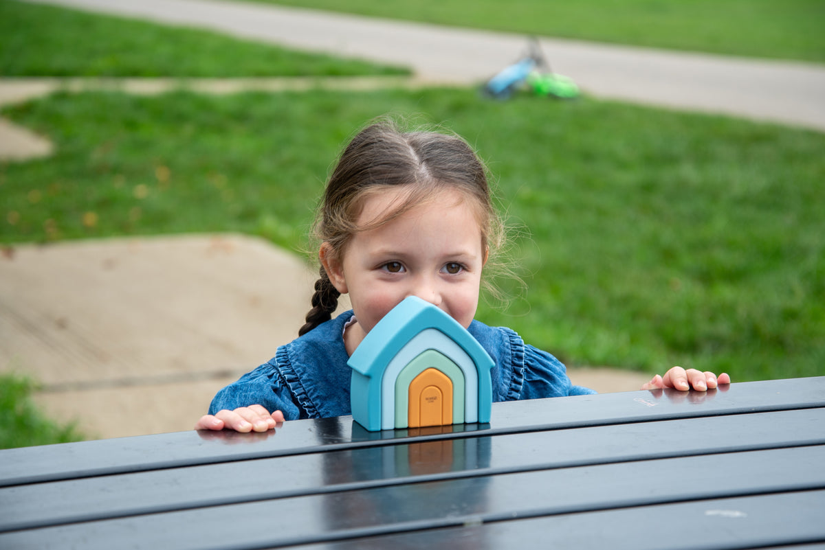 Child holding teal arch-top stacking house toy with orange door