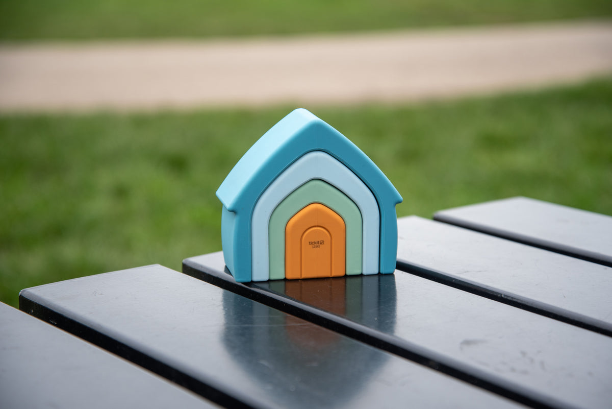 Blue stacking house toy with orange door and green inset on outdoor bench