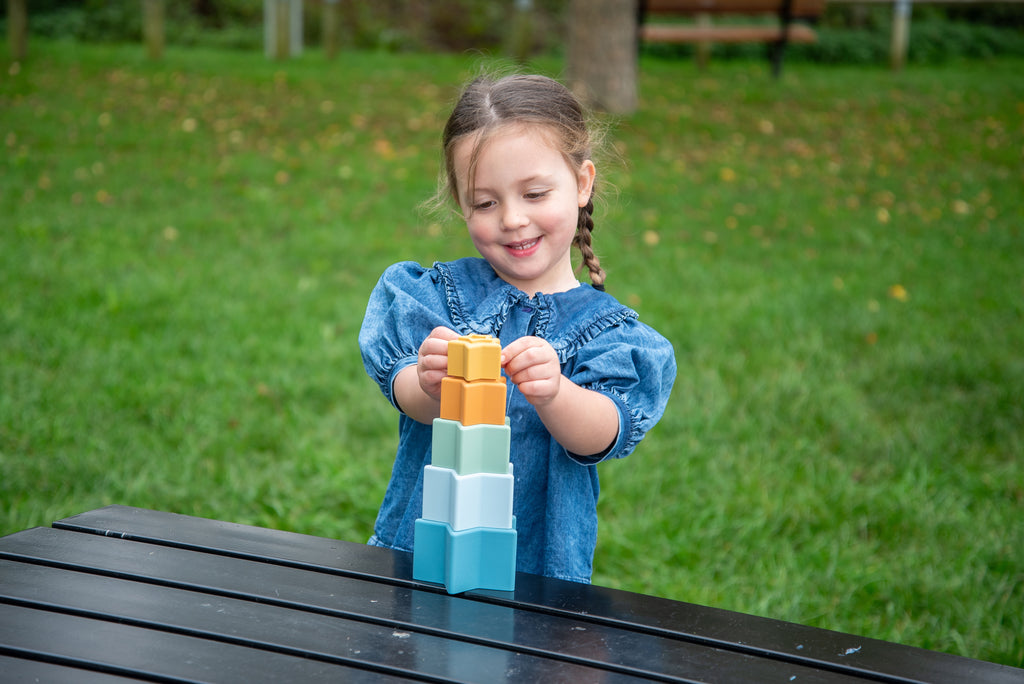 Child holding an orange star stacking cup with blue cups below