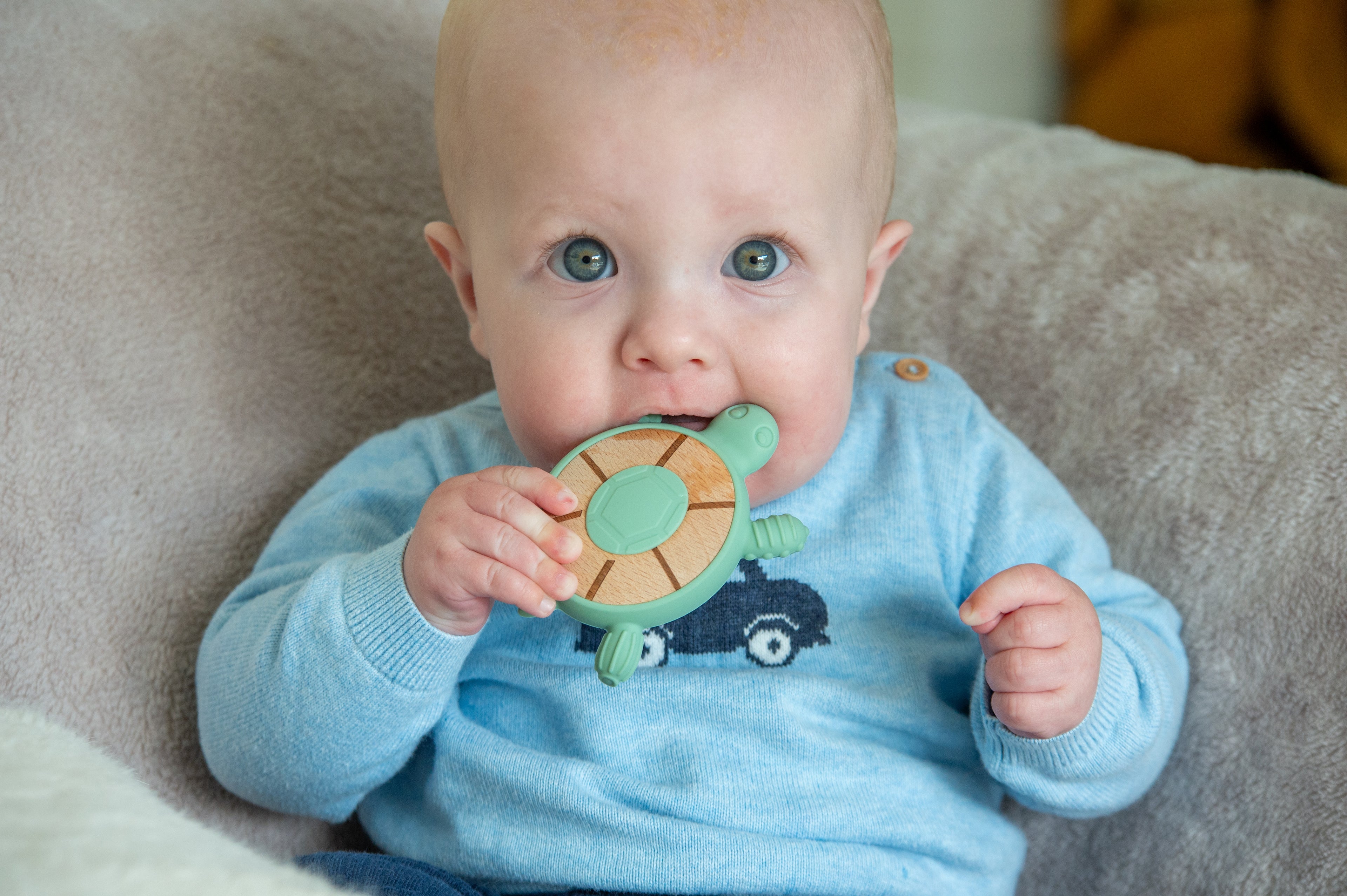 Baby in light blue outfit chewing mint turtle silicone teether