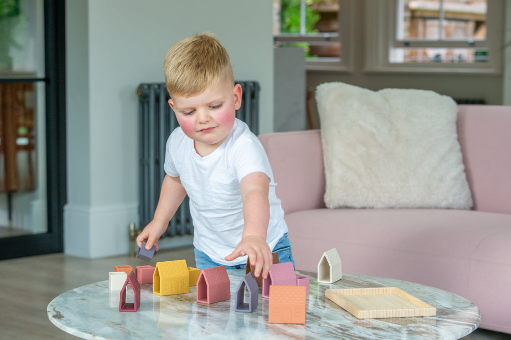 Toddler arranging house-shaped silicone blocks on a wooden village tray