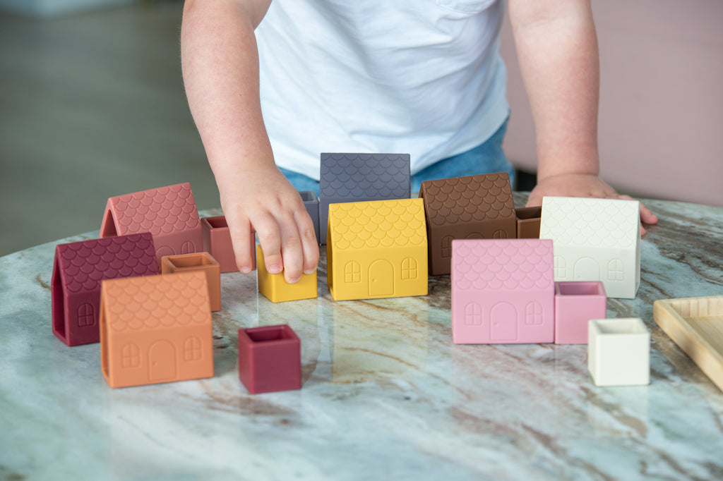 Assorted house-shaped silicone blocks on wooden tray with stacked cube pieces