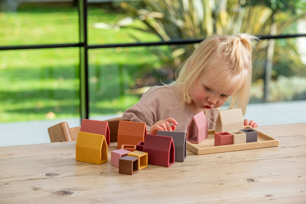 Child playing with house-shaped silicone village blocks on wooden base