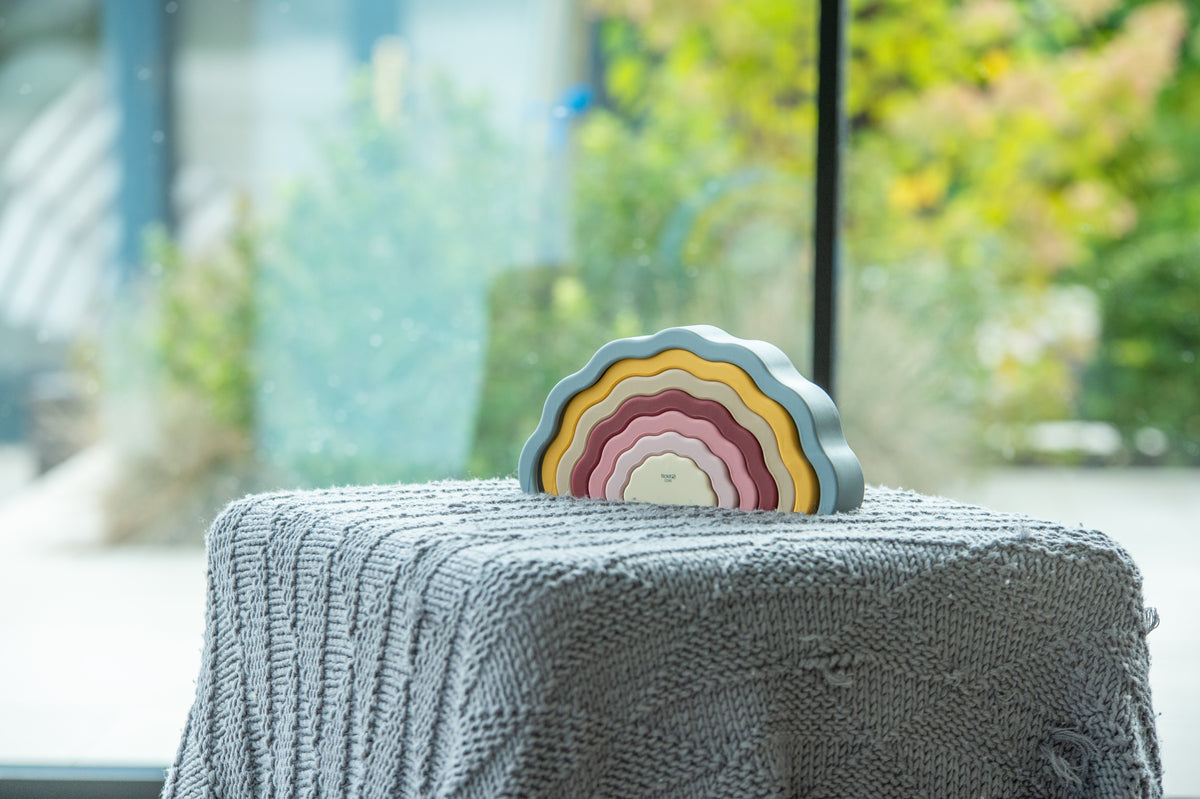 Layered rainbow earth wobble toy with curved tiers on a textured gray surface