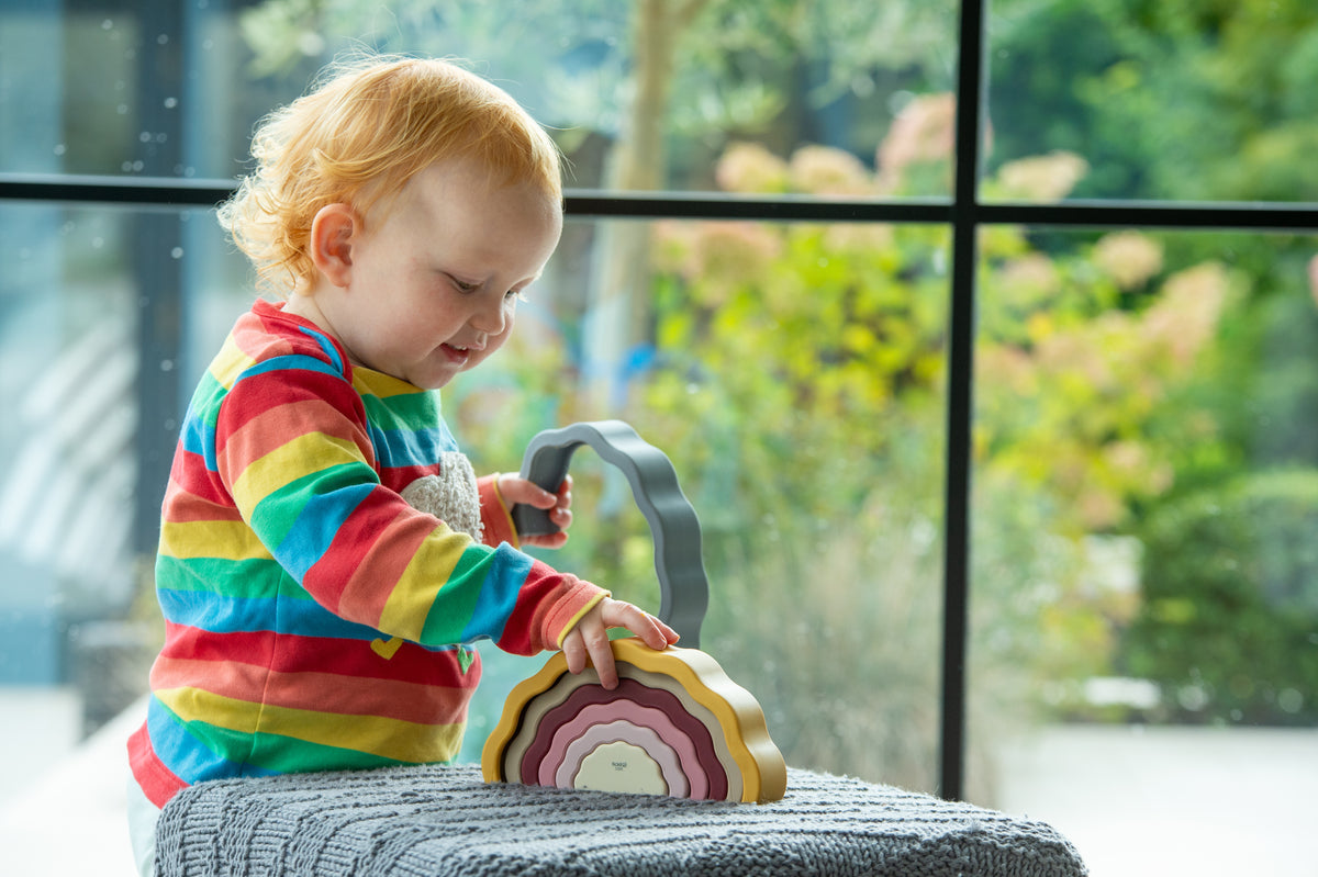 Rainbow layered earth stacking toy, small hands adjusting the wavy tiers