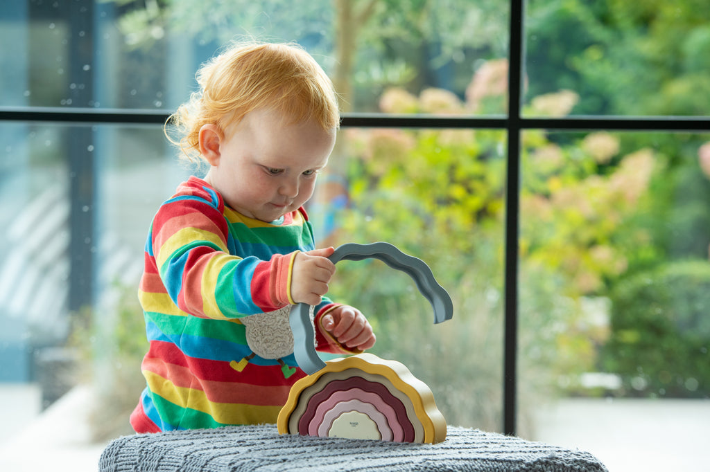 Rainbow earth wobble toy with curved tiered layers, gripped by small hands