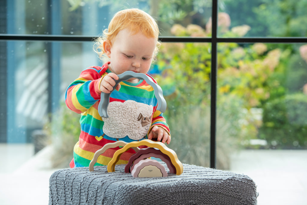 Rainbow earth stacking toy with wavy colored layers, held by a child