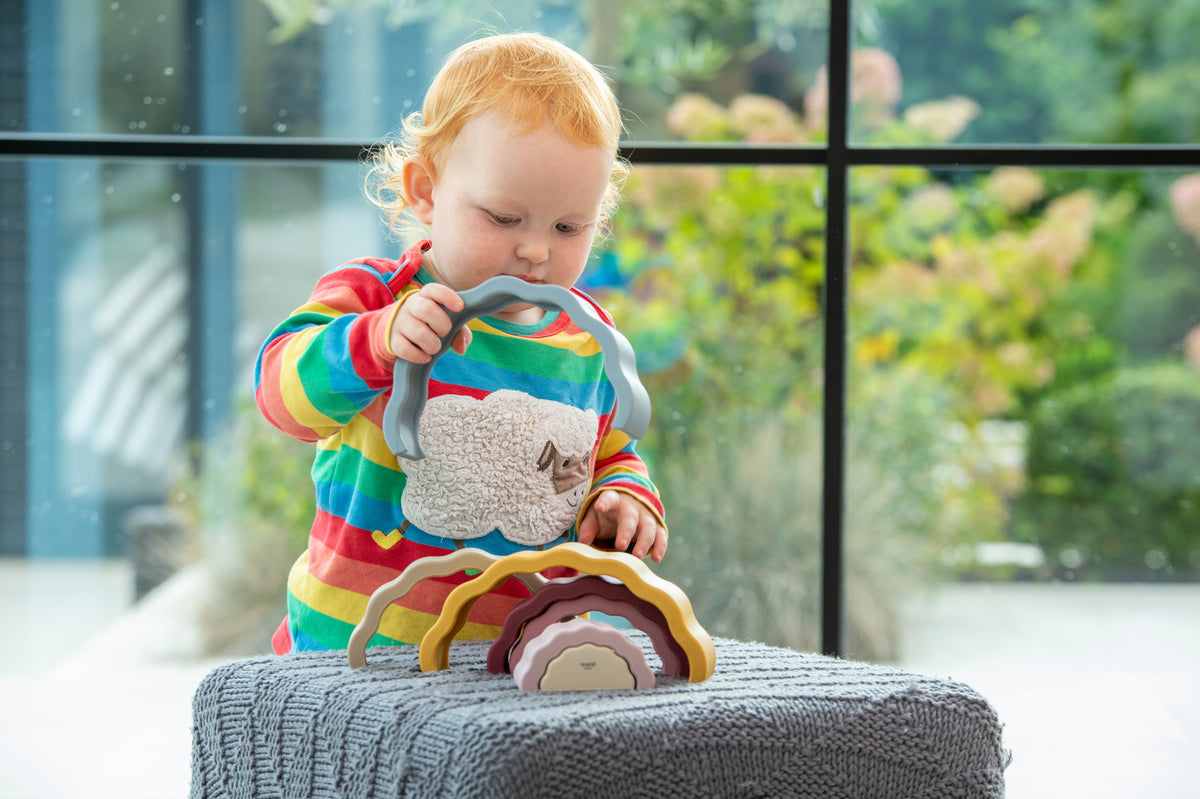 Rainbow earth stacking toy with wavy colored layers, held by a child