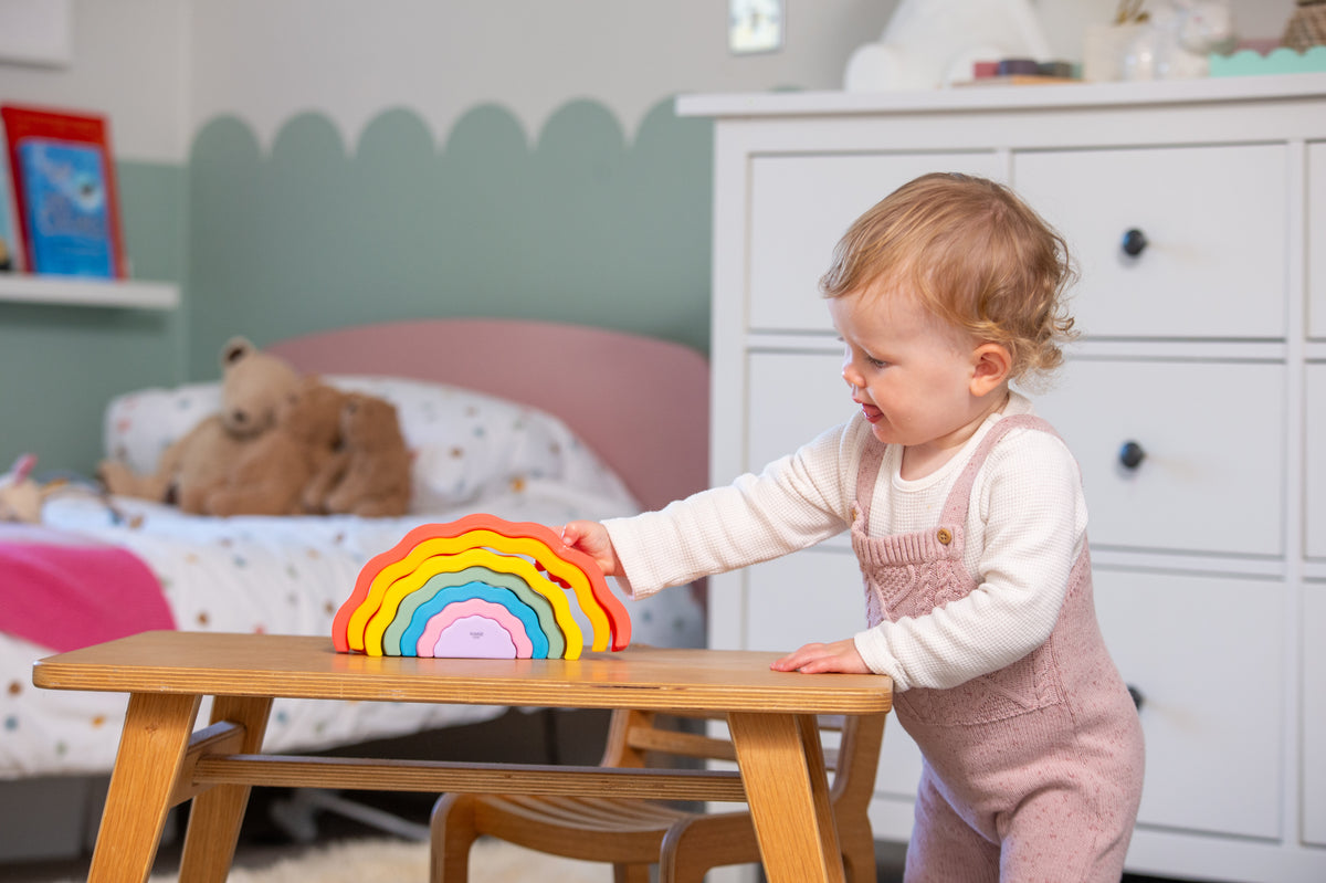 Rainbow wobble stack toy with multicolor arches on table, child reaching toward it