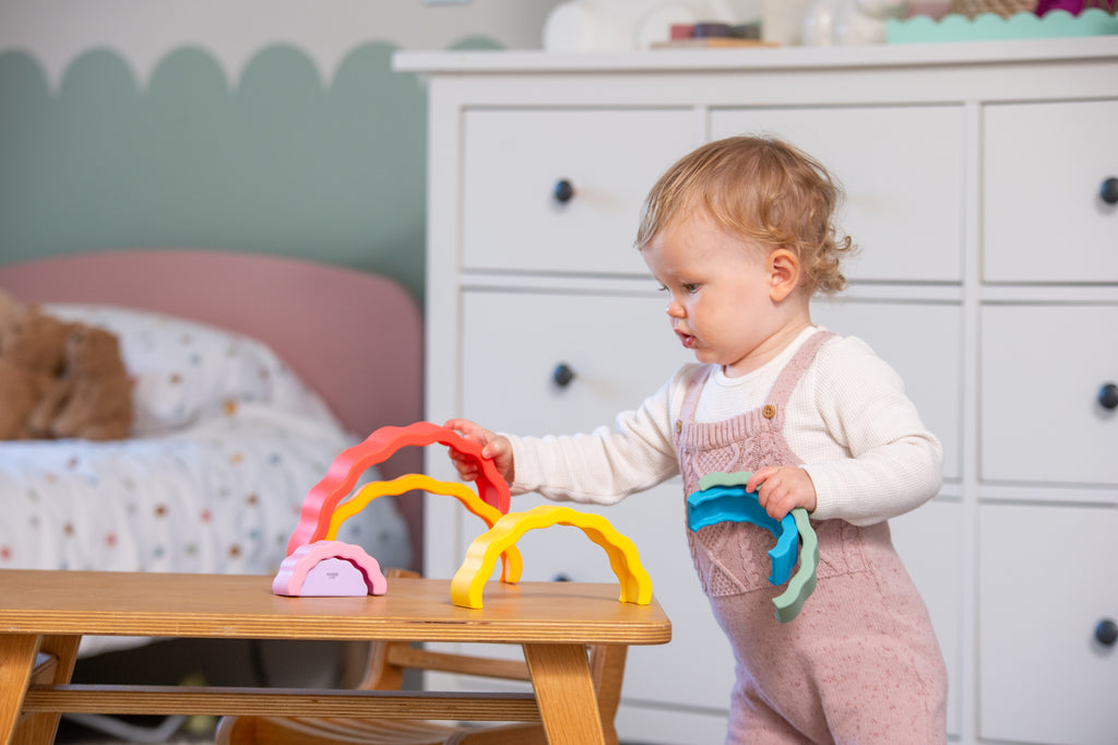 Rainbow wobble stack toy in multicolor arches on tabletop, child holding it