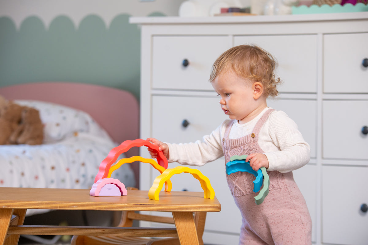 Rainbow wobble stack toy in multicolor arches on tabletop, child holding it