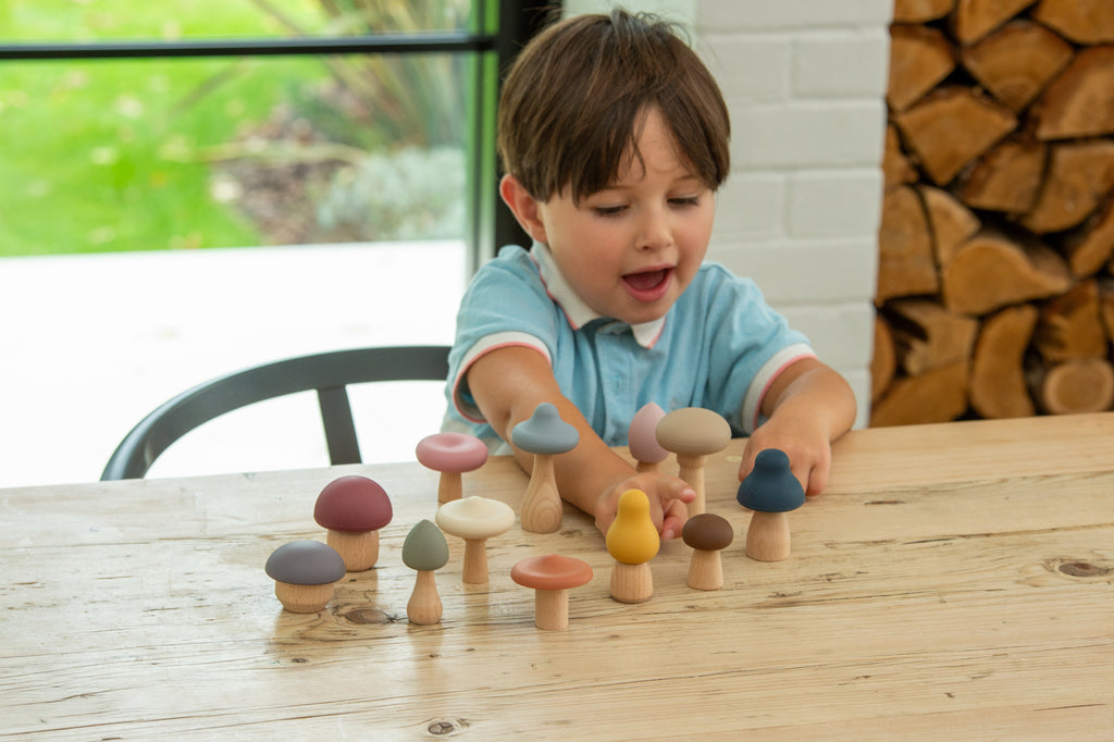 Child playing with wooden mushroom stacking pieces, assorted rounded caps and stems