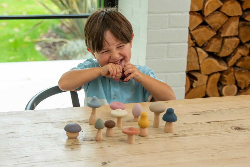 Child reaching for small wooden mushroom stacking pieces on a tabletop