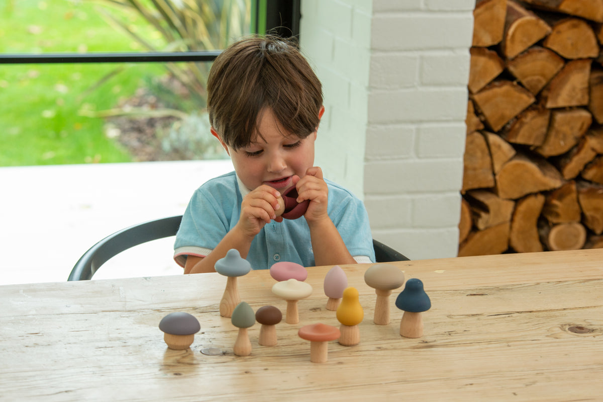 Child holding wooden mushroom stacking pieces while arranging pieces on a table