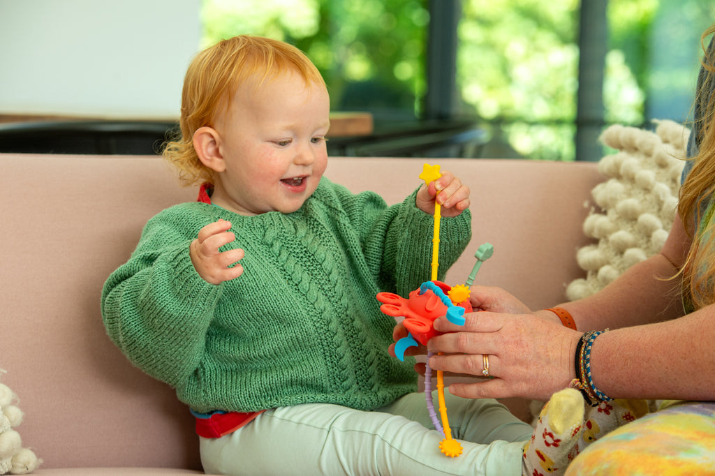 Toddler holding Silisoft rainbow zip pull toy, colorful star and zipper pulls visible