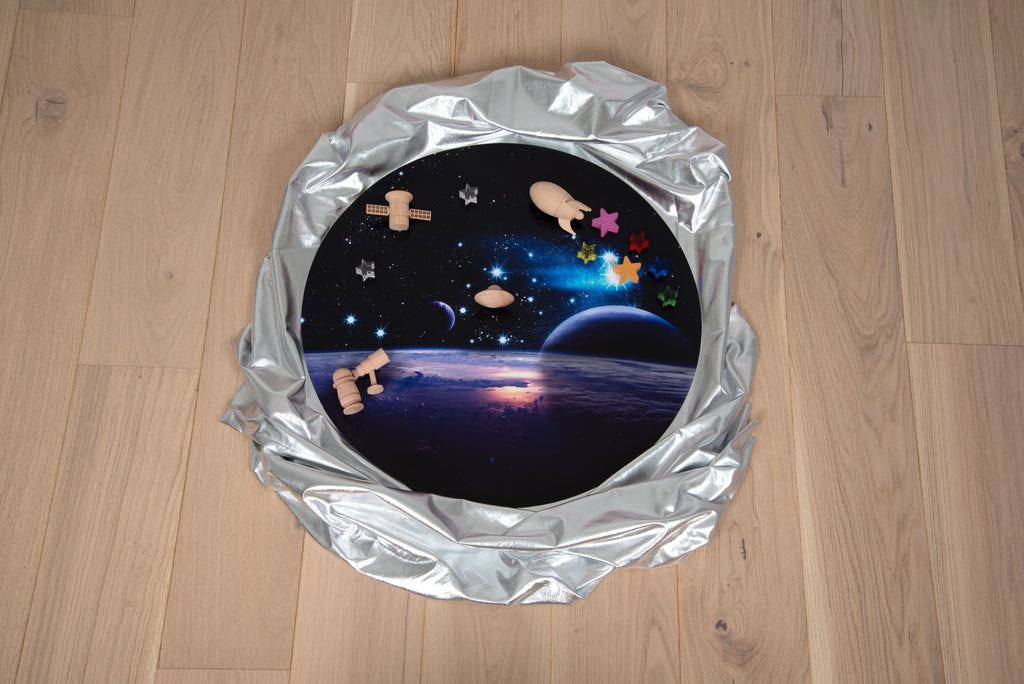Round space play mat with starry galaxy print and small toy pieces on top