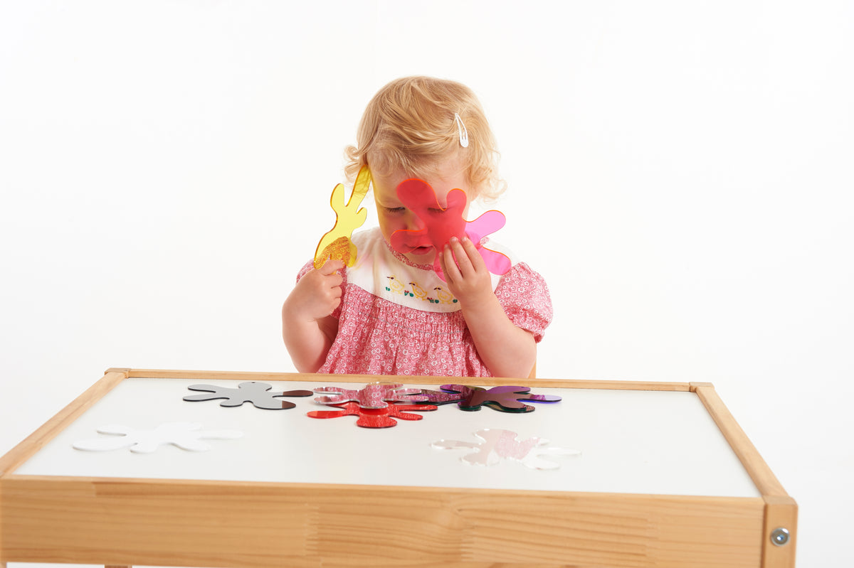 Toddler picking up red and yellow foam puzzle pieces at a wooden frame board