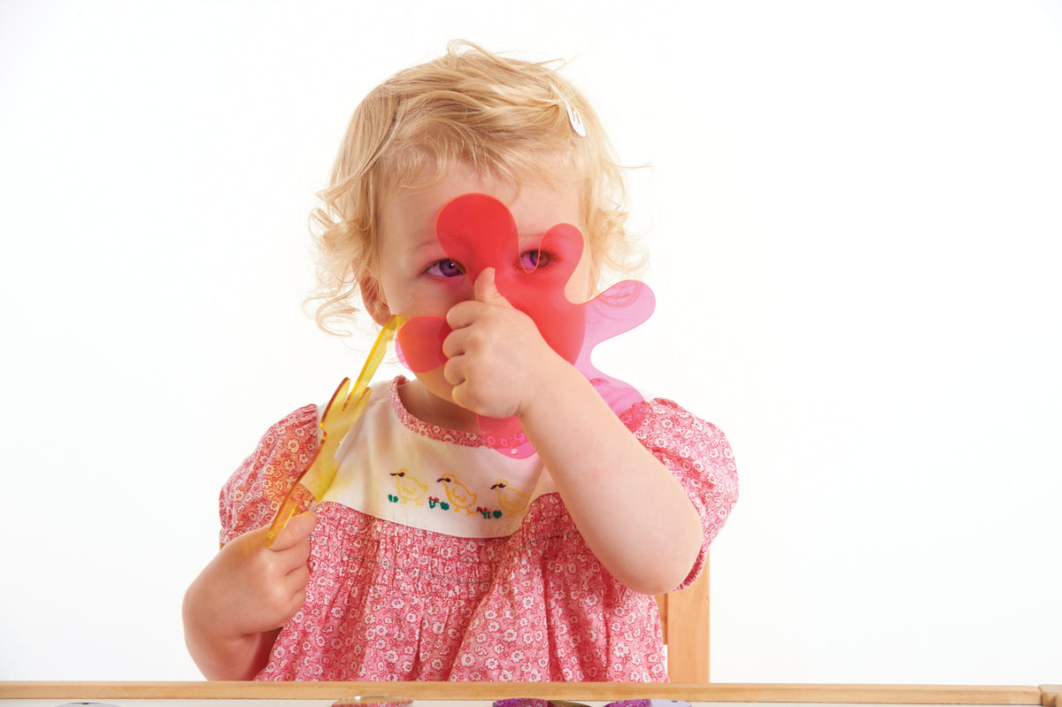 Toddler holding red and pink foam splash puzzle pieces above a wooden frame board