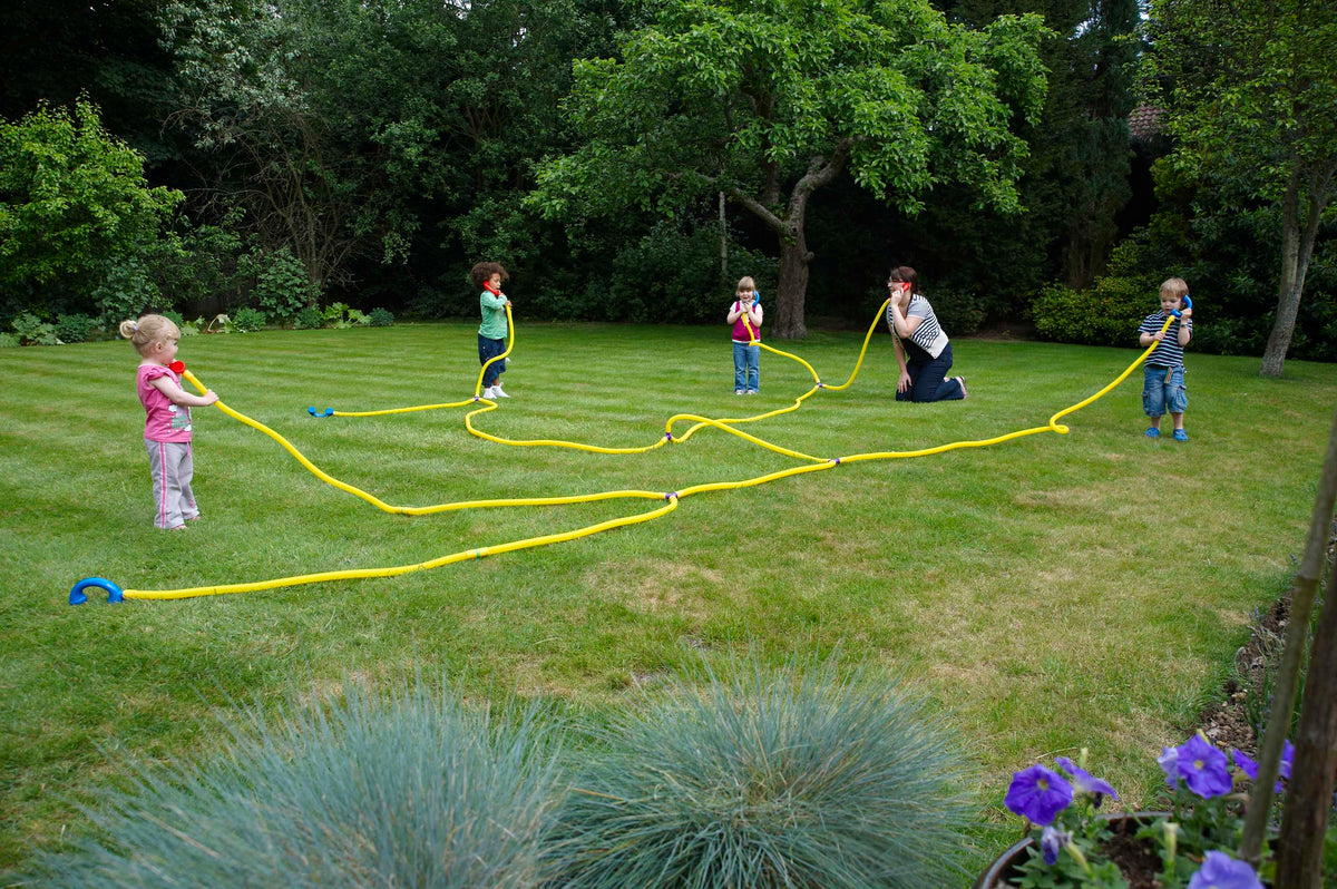 Outdoor play set of yellow talking tubes with blue ear pieces, stretched on a lawn