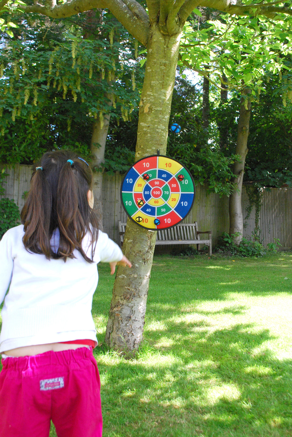 Outdoor number dartboard on a tree with a child standing and aiming