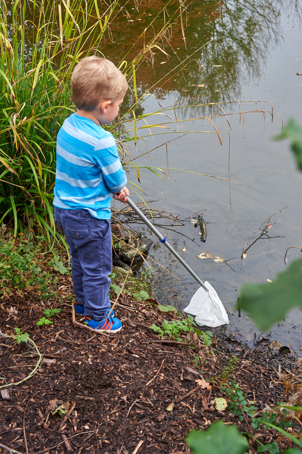Telescopic pond net with white mesh bag and silver handle, held by a standing child