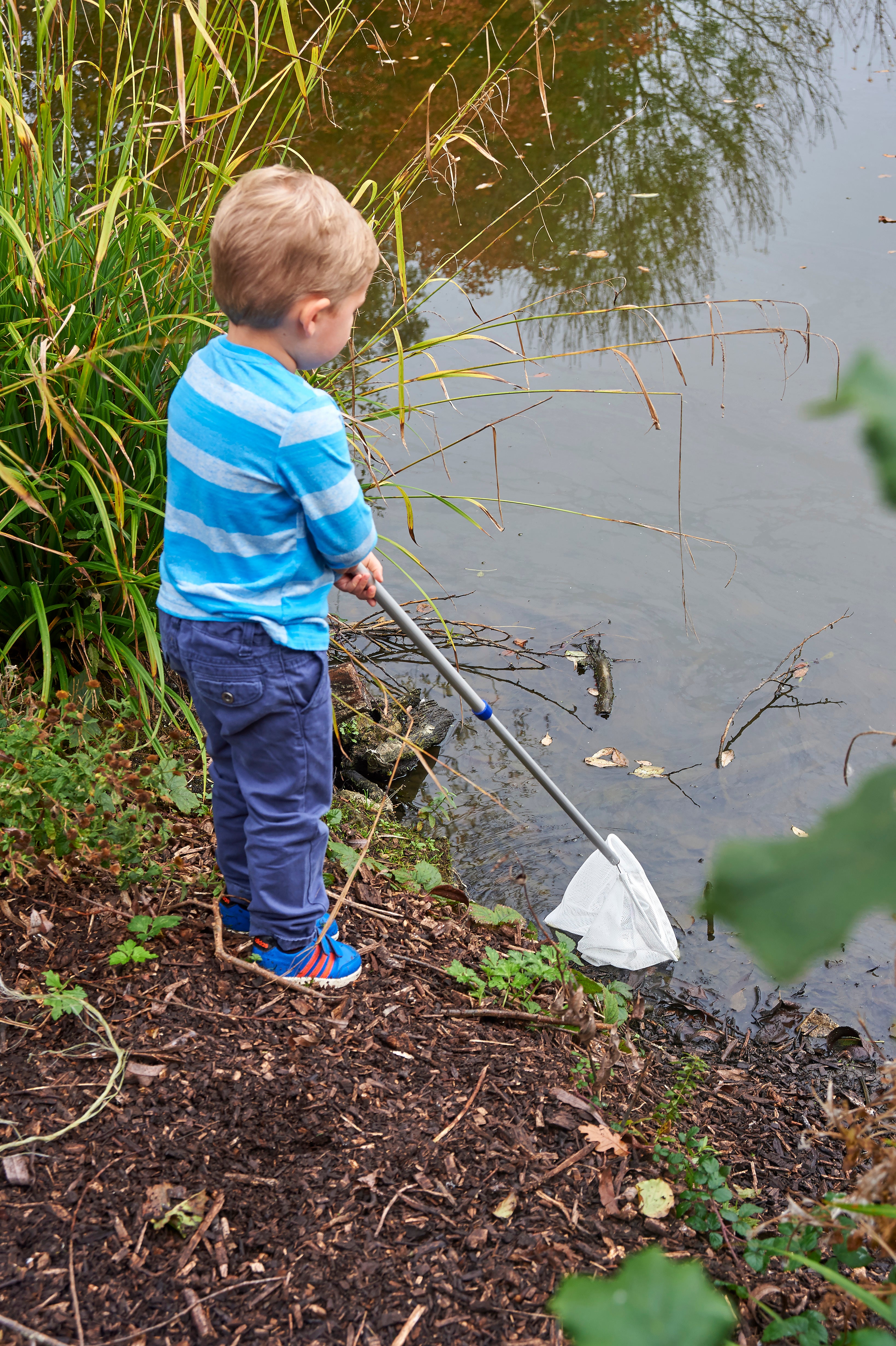 Telescopic pond net with white mesh bag and silver handle, held by a standing child