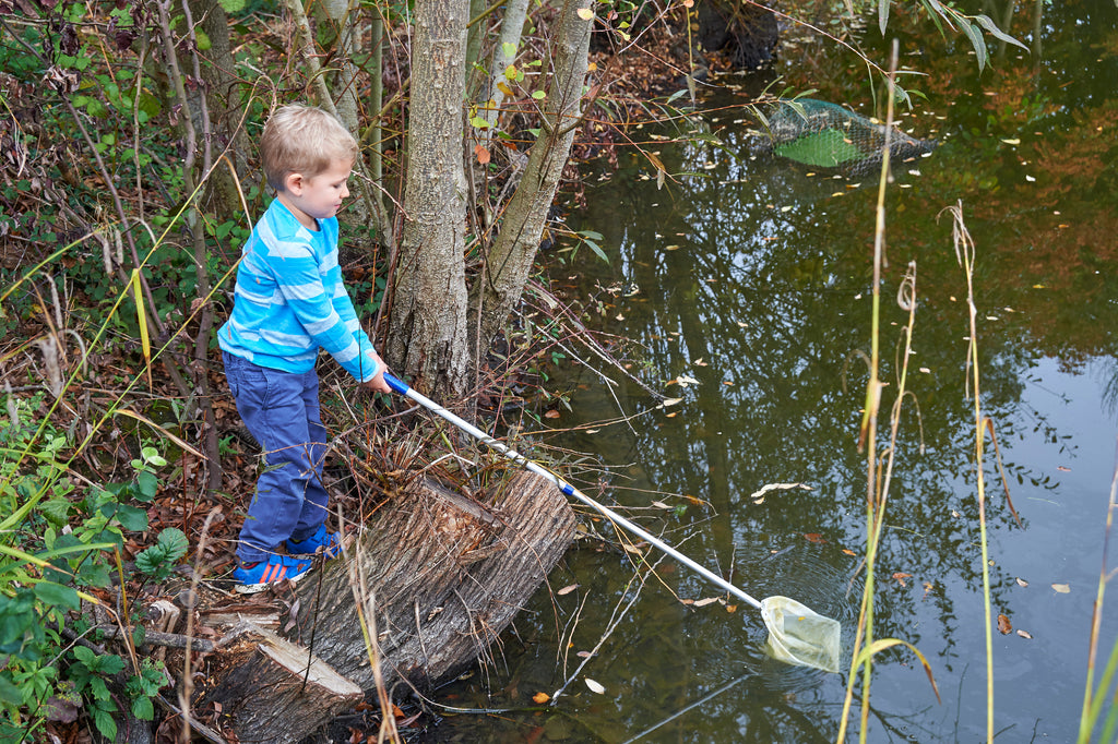 Telescopic pond net with white mesh scoop on a silver handle, angled toward pond water
