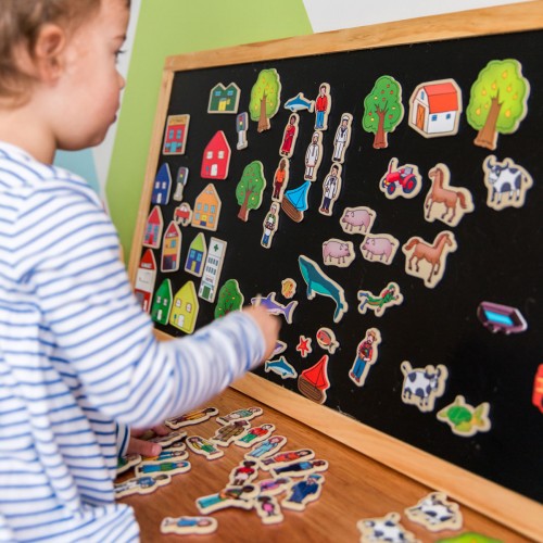 Magnetic board with colorful town, animal, and vehicle pieces on a black surface