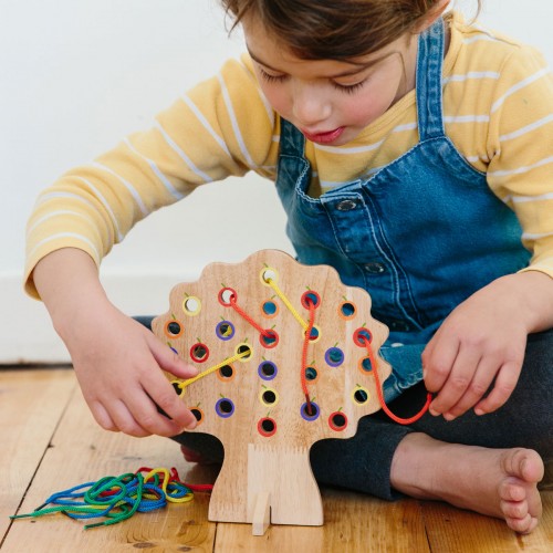 Wooden threading tree activity board with holes and colorful laces, held by hands