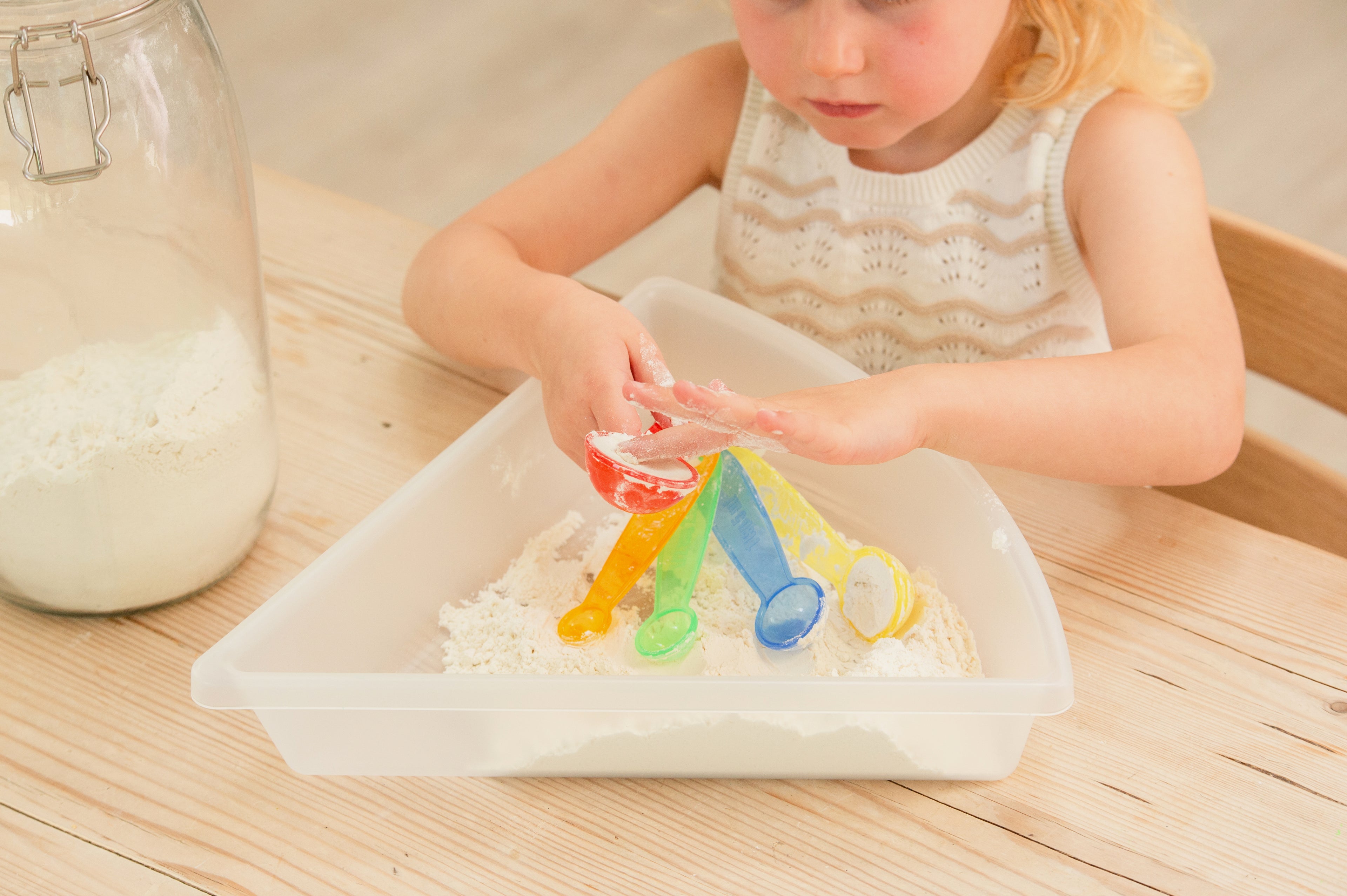 Translucent measuring spoons pouring colored powder onto a tray for kids.