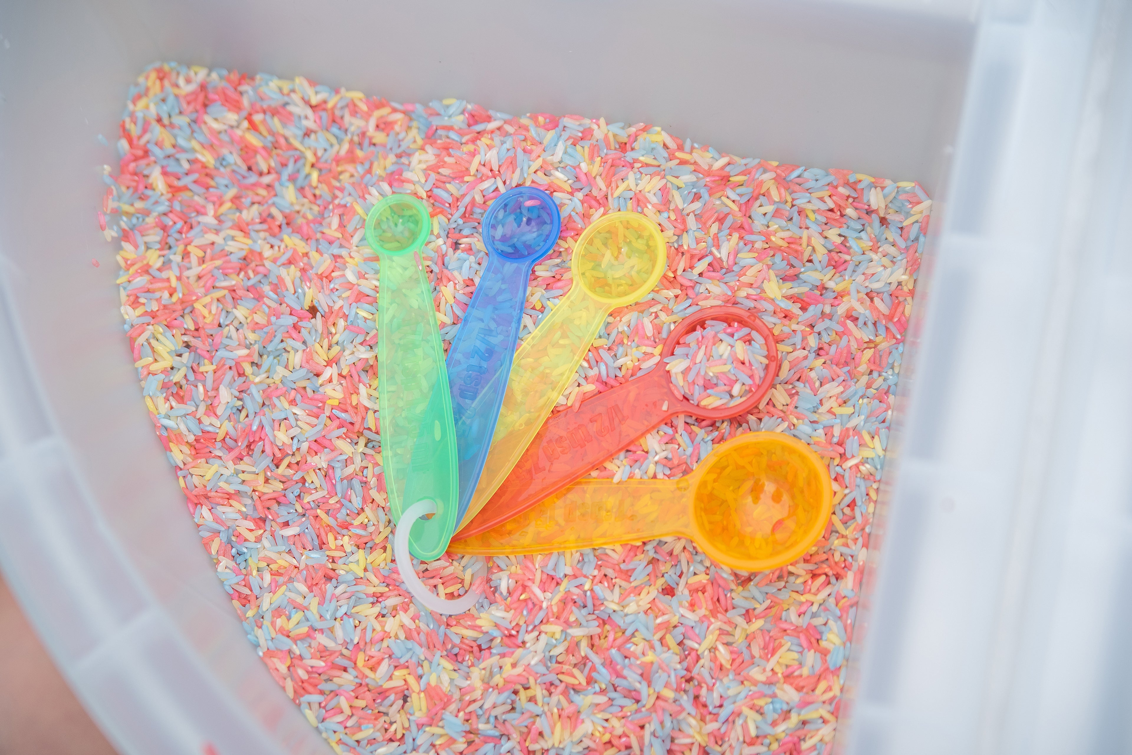 Translucent measuring spoon set resting in a container filled with colored sprinkles.