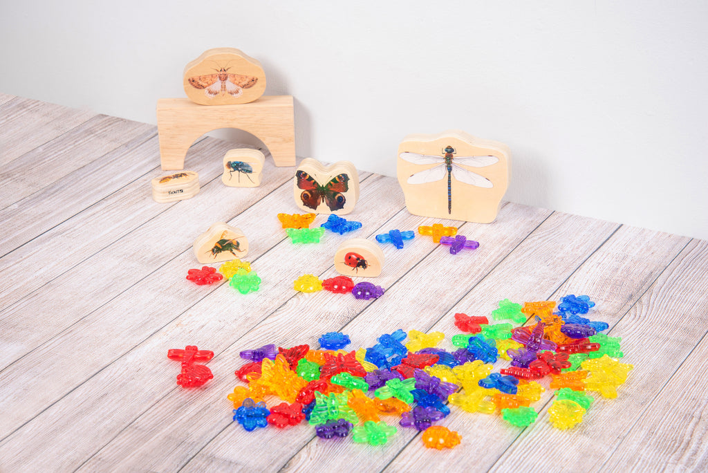 Translucent colorful bug pieces scattered on wooden activity boards and cards.