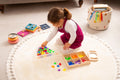Translucent colorful bug pieces with wooden sorting tray as a child plays on mat.