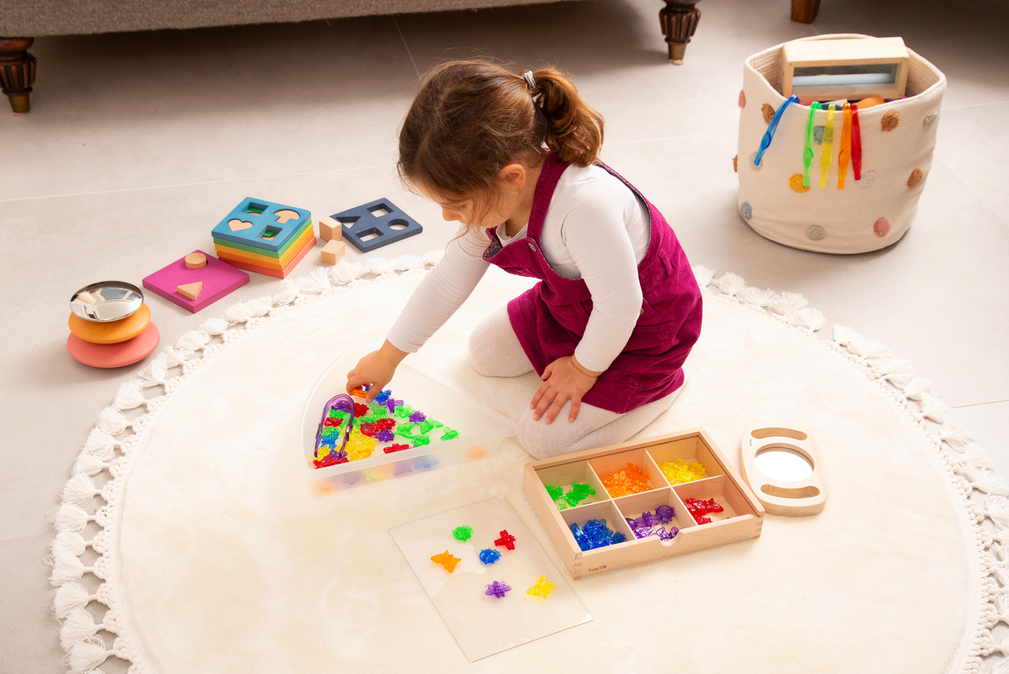Translucent colorful bug pieces with wooden sorting tray as a child plays on mat.