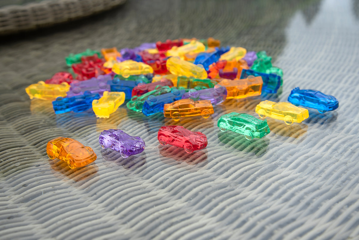 Scattered translucent toy cars in rainbow colors across a quilted surface