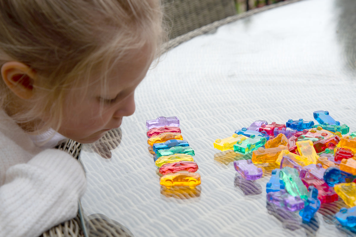 Translucent multicolor toy cars on a quilted surface near a child